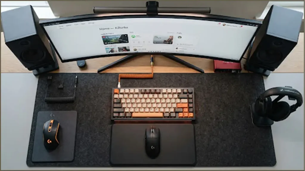 Top-down view of an organized gaming and workstation setup with a curved ultra-wide monitor, mechanical keyboard, wireless mice, and desk speakers